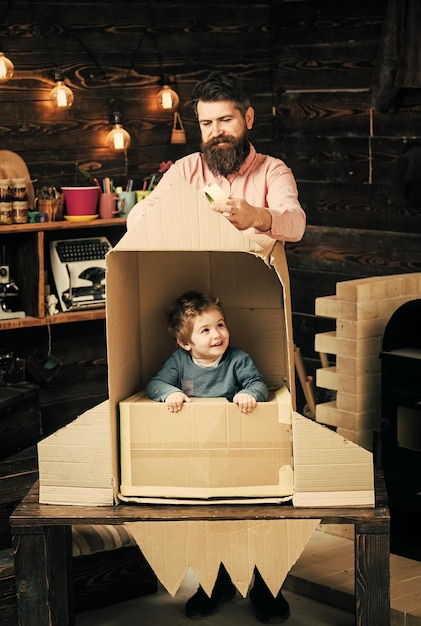 Photo kid happy sit in cardboard hand made rocket. parenthood concept. boy play with dad, father, little cosmonaut sit in rocket made out of cardboard box. child boy play cosmonaut, astronaut