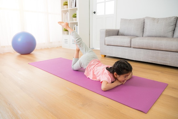 kid having fun doing some morning gymnastic with fitness stretching at home lying down on the floor with mat in the living room. family activity and healthy lifestyle concept.