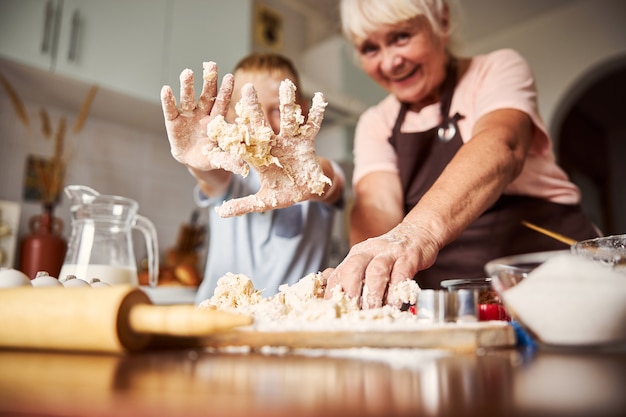 Kid having fun with making dough while cooking with grandma