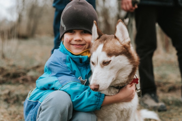 Kid and his friend husky siberian dog portrait little child boy hugging cute white brown mammal animal pet of one year old with blue eyes in autumn rustic and countryside nature forest