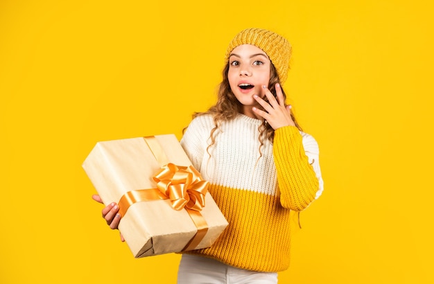 Photo kid little girl hold gift box with ribbon on yellow background. teen girl received holiday gift. best christmas gifts. child excited unpacking gift. christmas present for daughter. enjoy surprises.