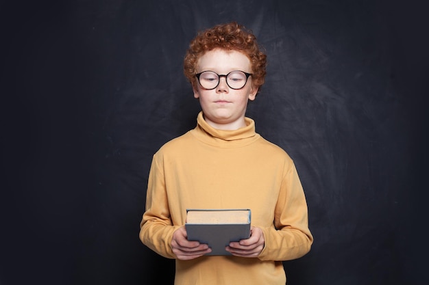 Photo kid looking at book on school blackboard background