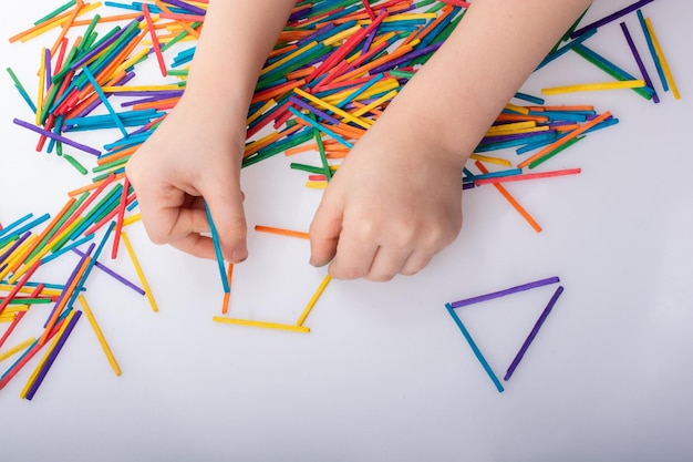 Kid making geometric shapes with colorful sticks on white background