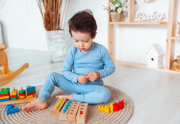 A kid in pajamas is sitting on the floor in his room and playing with a wooden construction kit natural toys for children the boy is playing in his bedroom