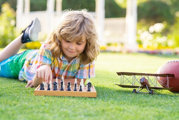 Photo kid playing chess game in backyard laying on grass concentrated child play chess kid playing board game outdoor