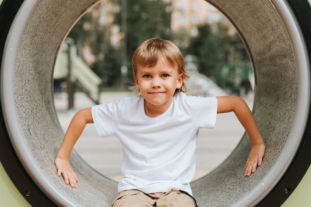 Kid playing on the city playground on ring around cute little happy smiling candid five year old child boy with long blond hair in a white tshirt generation z children mental health lifestyle