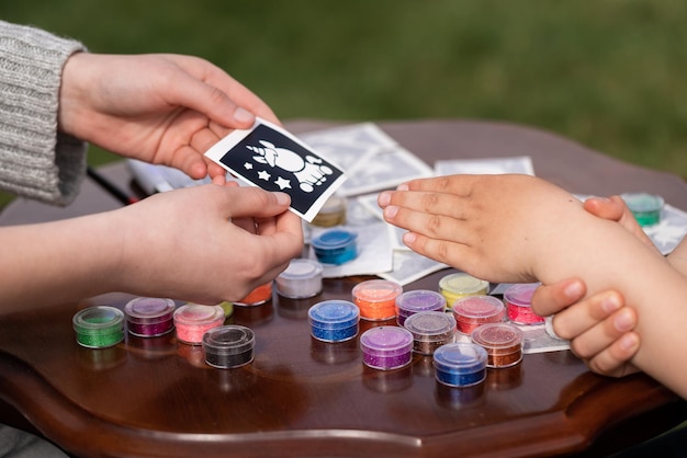 Kid's animator is creating a Shimmering sparkling glitter tattoo on a child's hand at a birthday party