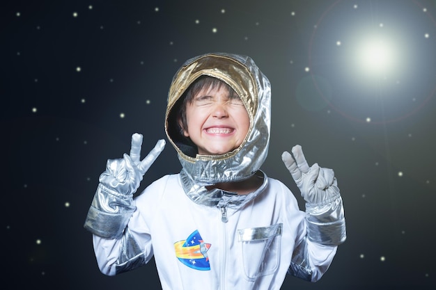 Photo a kid in a silver space suit smiles and makes peace signs concept of imagination and play