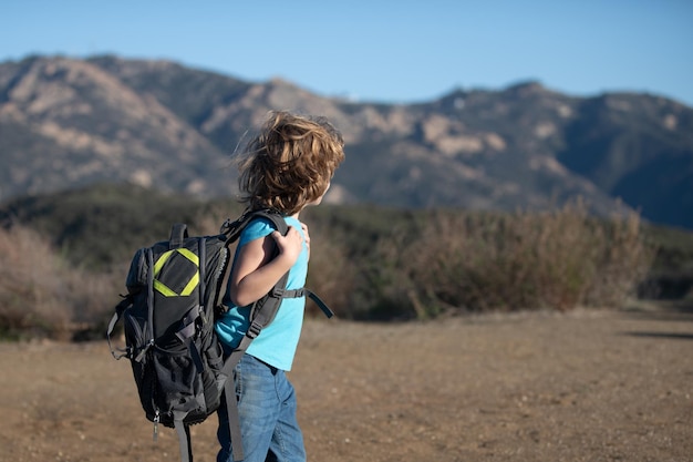 Kid with backpack hiking in scenic mountains Boy local tourist goes on hike