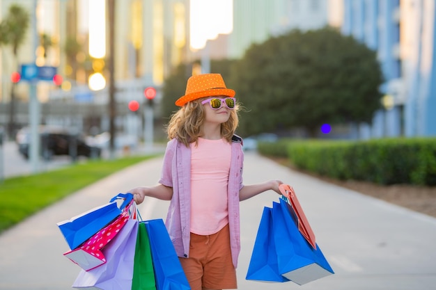 Photo kid with many shopping bags outdoor cute little boy in summer fashion kids clothes with shopping bags walking on street purchases sale and consumer concept