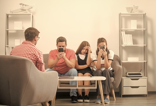 Kid with phone addicted daddy and mom sitting at psychologist solving problem family