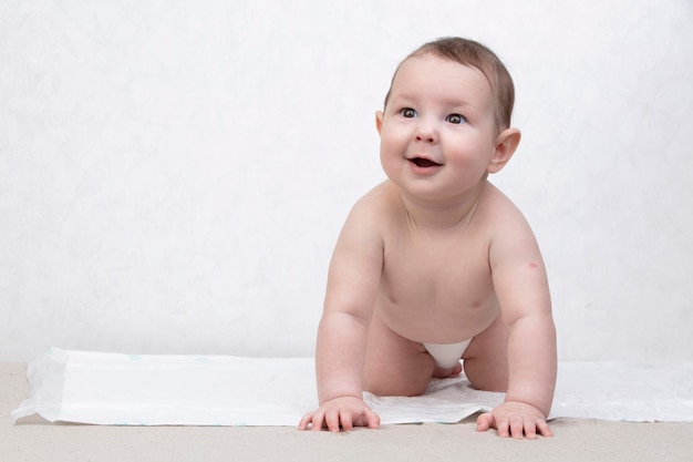 Kid with a smile on a white background A happy six month old boy crawls on the bed and laughs