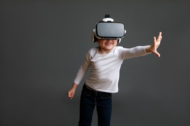 Kid with virtual reality headset,  shot isolated on grey surface. Child exploring digital virtual world with VR goggles.