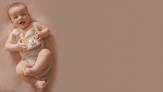 Kid with a wooden camera lies on a beige background