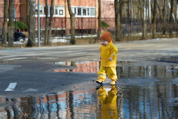 A kid in a yellow waterproof suit walks through puddles