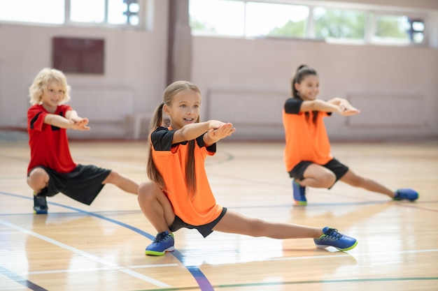 Photo kids exercising in the gym and doing lungings to the left