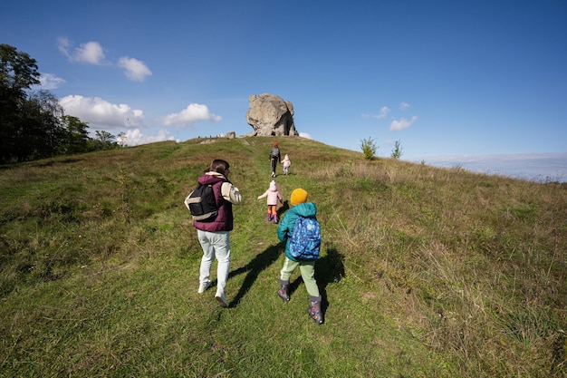 Kids exploring nature Children wear backpack hiking with mother near big stone in hill Pidkamin Ukraine