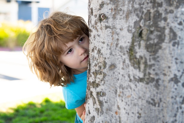 Kids games playing hide and seek peekaboo little boy hiding by tree