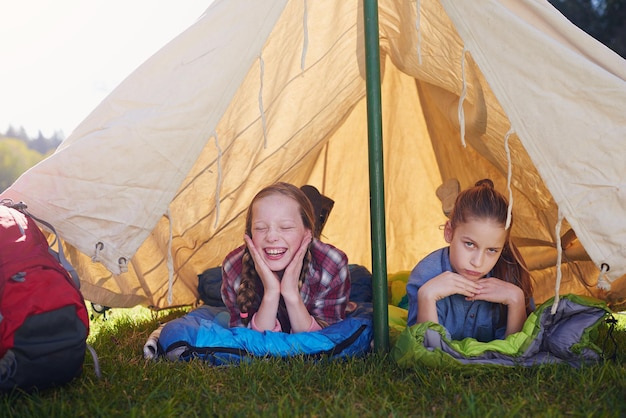 Kids gen z and camping in tent in nature for holiday adventure and sleeping in woods for vacation Portrait happiness and friends on field trip for school children and bootcamp for girls