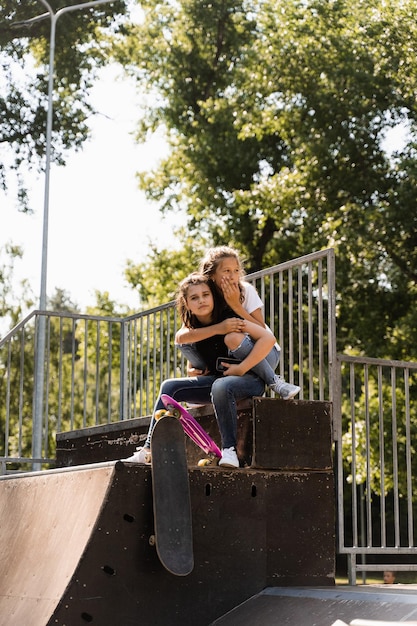 Kids girls smile and laugh and have fun together Children with skateboard and penny boards communicate and discuss on the sports playground Girls friendship concept