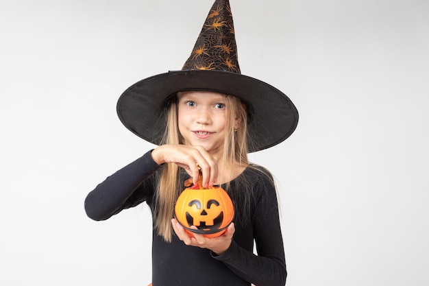 Kids Halloween A beautiful cute girl in a witch costume wearing a hat takes out candy from a basket in the shape of Jack's lantern