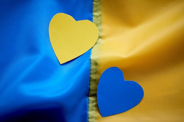 Kids hands holding yellowblue paperhearts on Ukrainian flag background