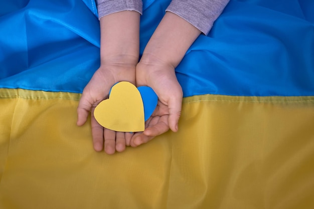 Kids hands holding yellowblue paperhearts on Ukrainian flag background