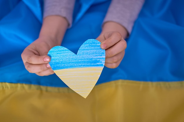 Kids hands holding yellowblue paperhearts on Ukrainian flag background