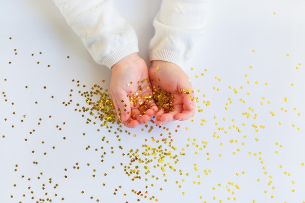 Kids hands keep gold star sprinkles on light backgound Christmas magic and celebration Festive atmosphere holiday concept birthday Top view