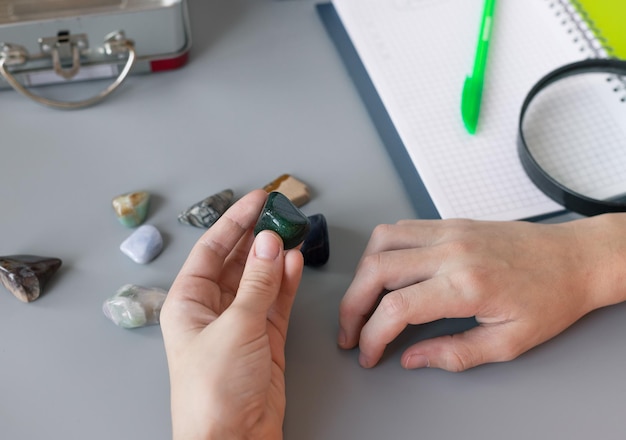 Kids hands studying semiprecious stones on gray desk with supplies Mineral stones collection