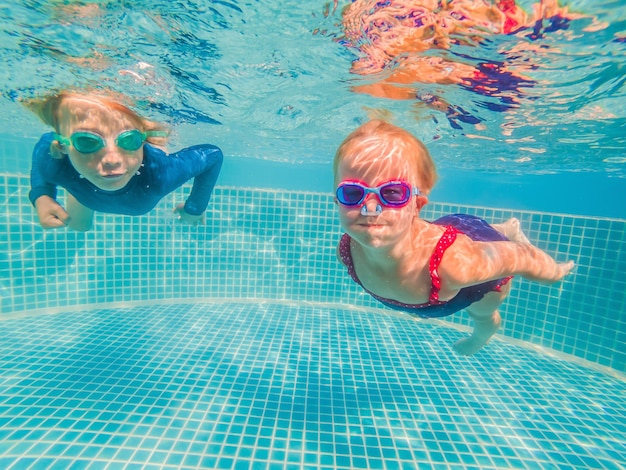 Kids having fun playing underwater in swimming pool on summer vacation