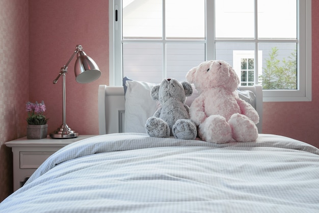 Kids room with dolls and pillows on bed and bedside table lamp