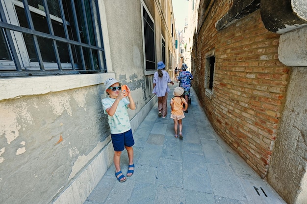 Kids walk narrow brick streets in Venice Italy Boy tourist making photo by phone