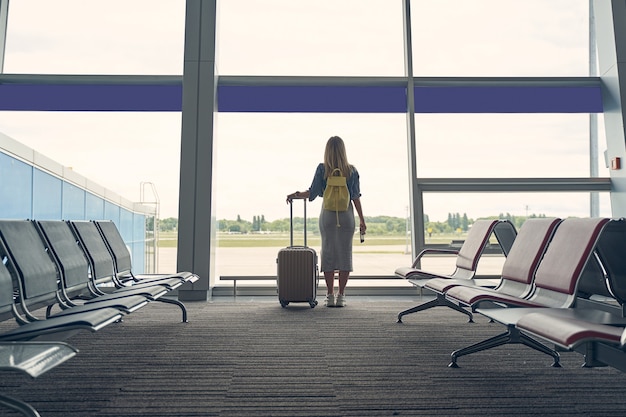 Kind blonde woman keeping rucksack on her back and spending her morning in the departure lounge