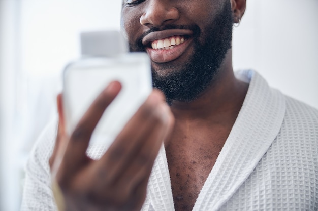 Kind dark-skinned male person feeling happiness while preparing for romantic date, wearing bathrobe