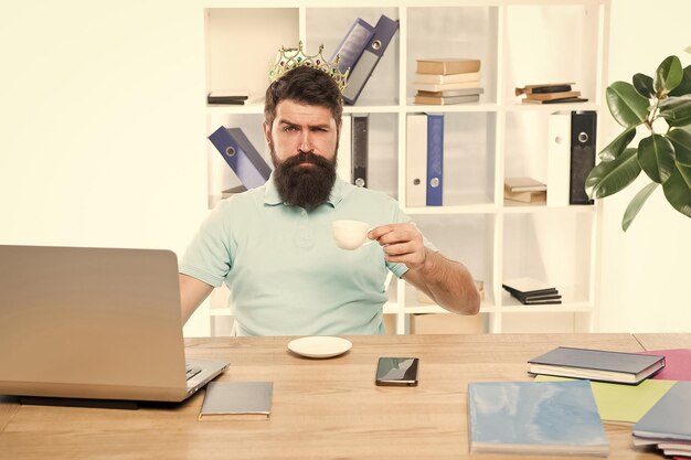 King of office Head of department Head office concept Man bearded manager businessman entrepreneur wear golden crown on head Relaxed top manager drinking coffee Confident boss enjoying his glory