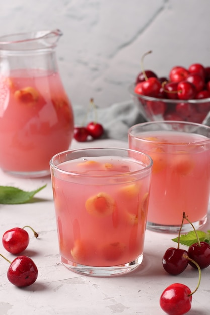 Kissel with sweet cherries in two glasses and jug on gray surface, Vertical format, Closeup