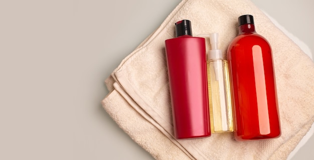 Kit of shampoo, conditioner and cleansing oil lying on a bath towel in a bathroom. Space for text