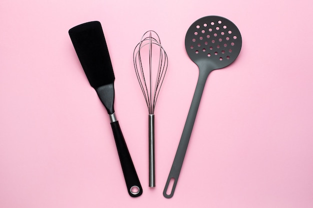 Kitchen accessories spatula whisk on a pink background