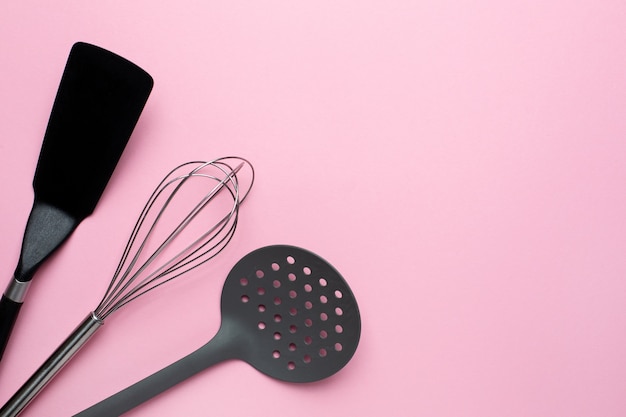 Kitchen accessories spatula whisk on a pink background