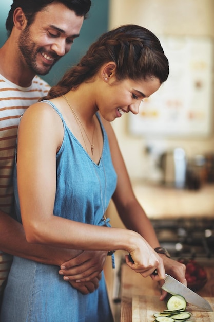 Kitchen couple and hug with knife cucumber and food cutting in home with smile love and care Cooking salad and vegetable with happy people with bonding support and marriage with wellness