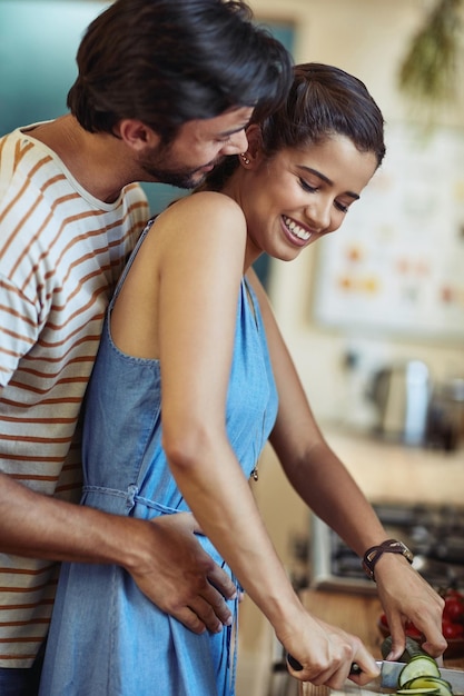 Kitchen couple and hug with smile knife and food cutting in home with vegetable love and care Cooking salad and cucumber with happy people with bonding support and marriage with wellness