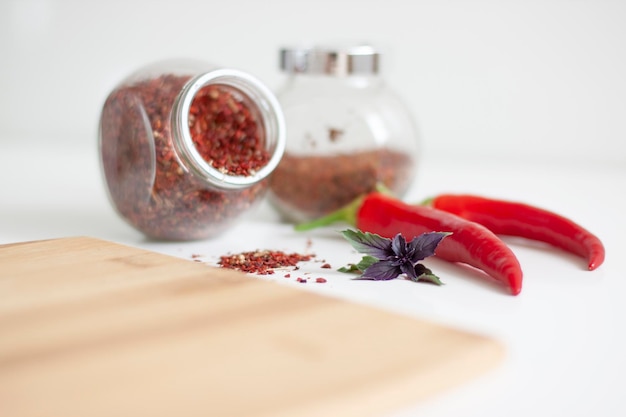 A kitchen cutting board in the foreground ingredients in the background Pepper basil spices