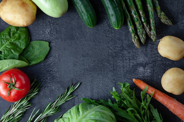 Kitchen - fresh colorful organic, eco young spring vegetables on dark stone background. Carrots, tomatoes, parsley, asparagus and rosemary flat lay. Top view vegan food. Ingridients with copy space