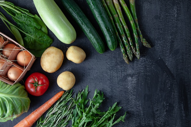 Kitchen - fresh colorful organic, spring vegetables on dark stone background. Carrot, tomato, parsley, asparagus and rosemary flat lay. Top view vegan food. Ingridients with copy space. Green cocnept