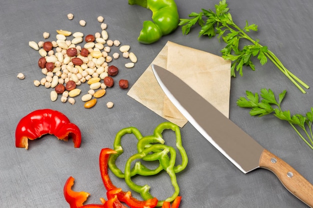 Kitchen knife and chopped green and red pepper nuts and chickpeas parsley sprigs