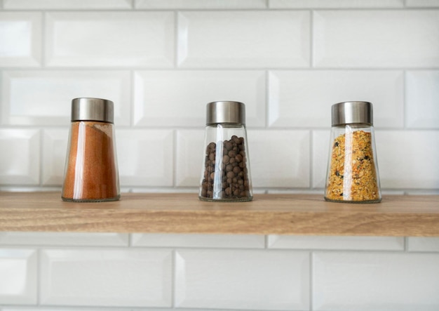 kitchen seasonings and spices in small glass jars on a kitchen countertop with a brick white wall