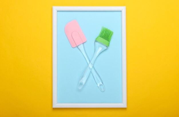 Kitchen spatula and brush on yellow surface with photo frame