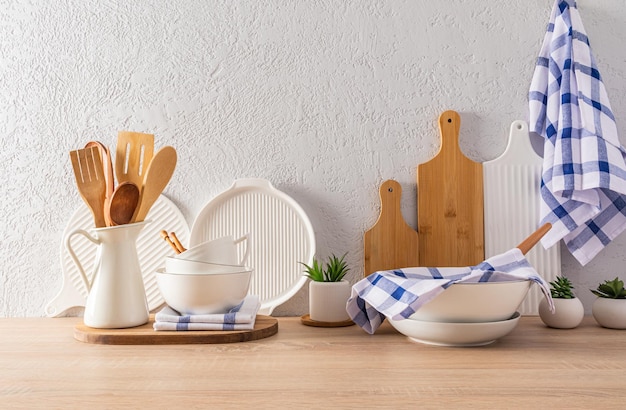 Kitchen utensils and utensils on a wooden countertop opposite the grey cement wall interior of a modern kitchen space in light colors