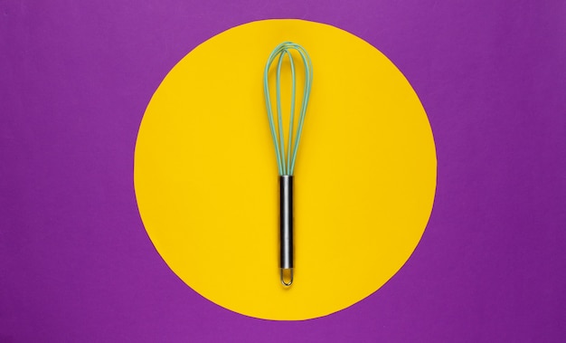 Kitchen whisk on purple with yellow color circle in the middle